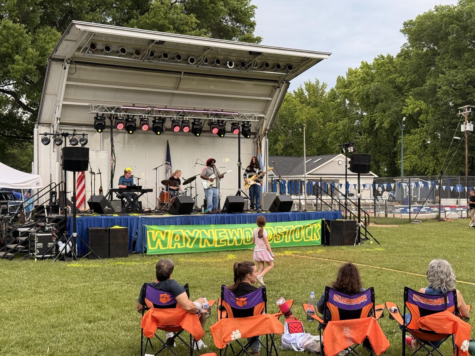 Wide view of the Waynewoodstock 2026 main stage with the WAYNEWOODSTOCK banner, families in lawn chairs, and a band on stage