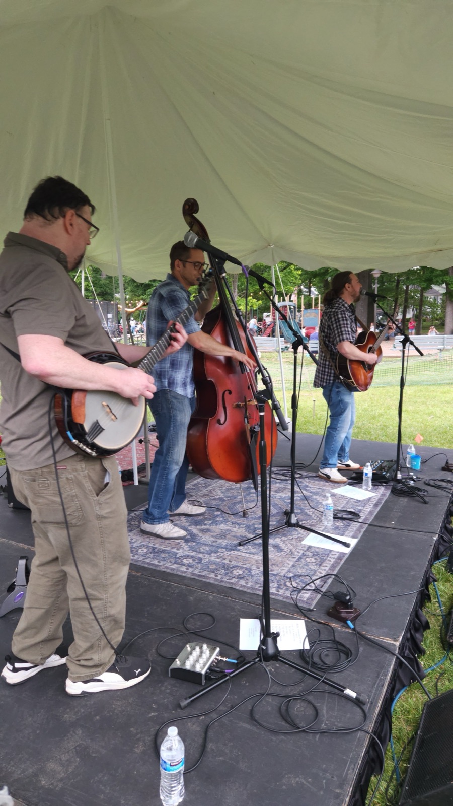 Bluegrass set under the tent stage at Waynewoodstock 2026 — banjo, upright bass, and acoustic guitar