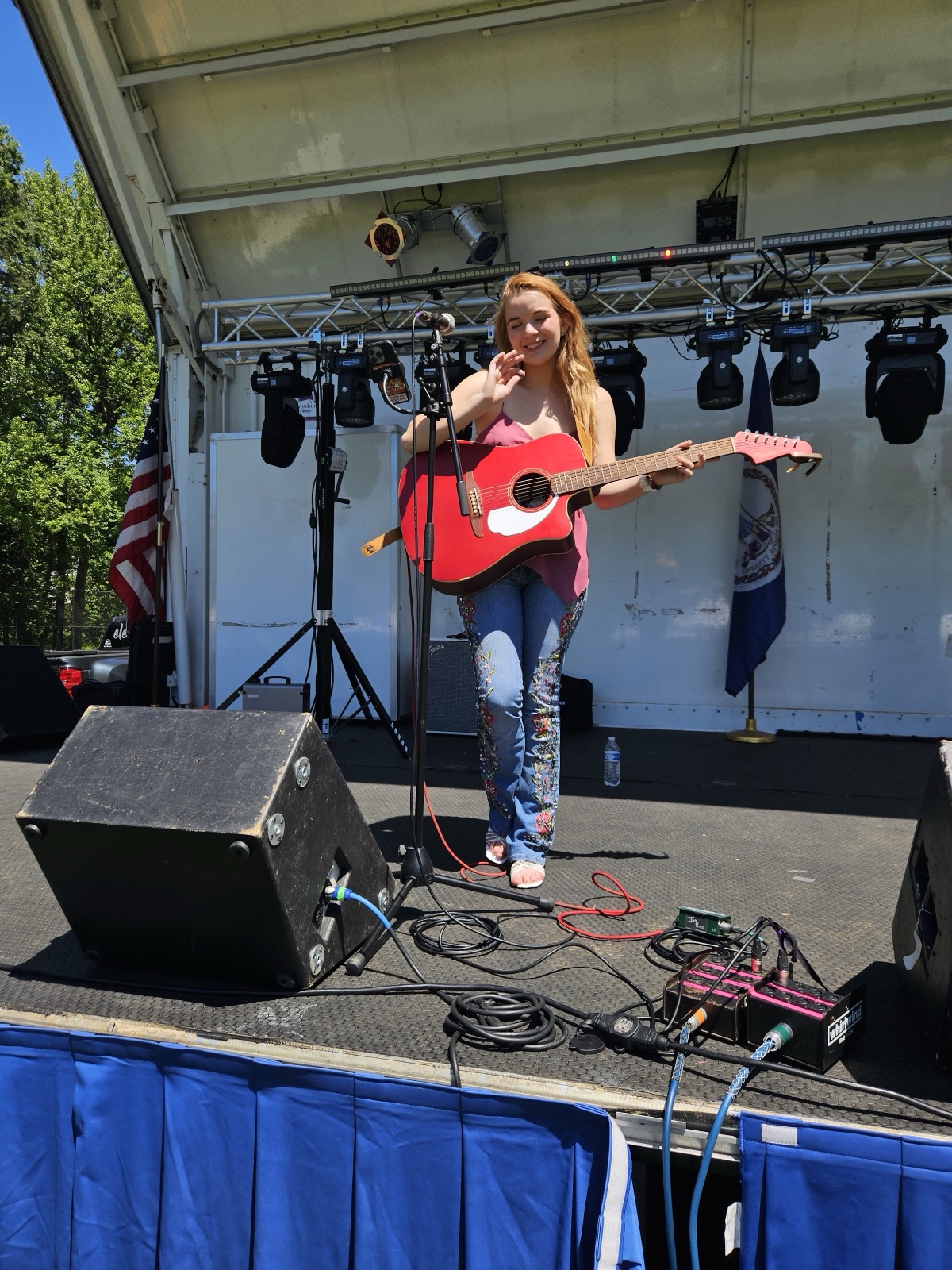 Solo singer with a red acoustic guitar performing on the Waynewoodstock 2026 main stage in front of the Virginia flag